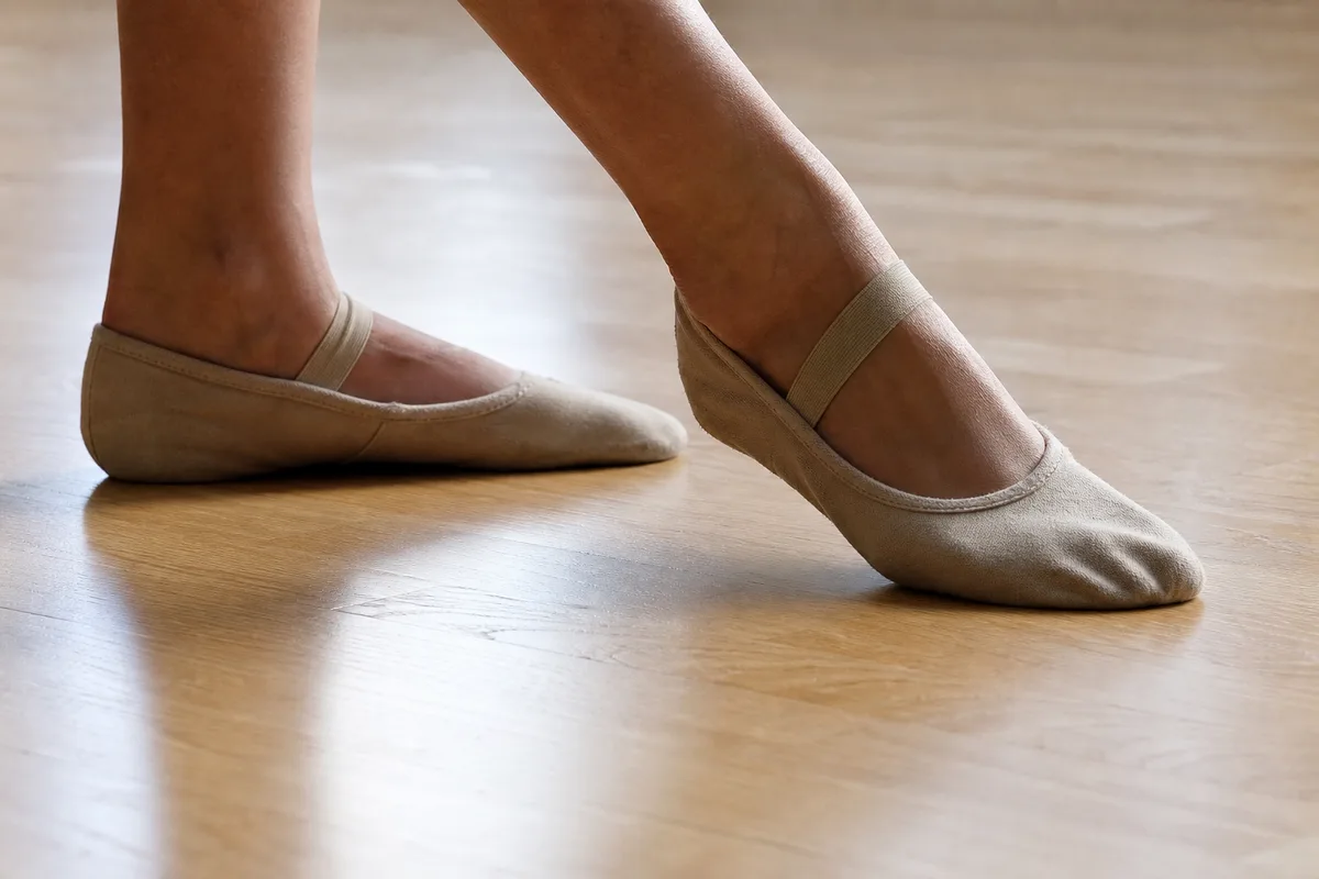Pieds en chaussons de danse effectuant un cercle de cheville au sol sur un parquet clair