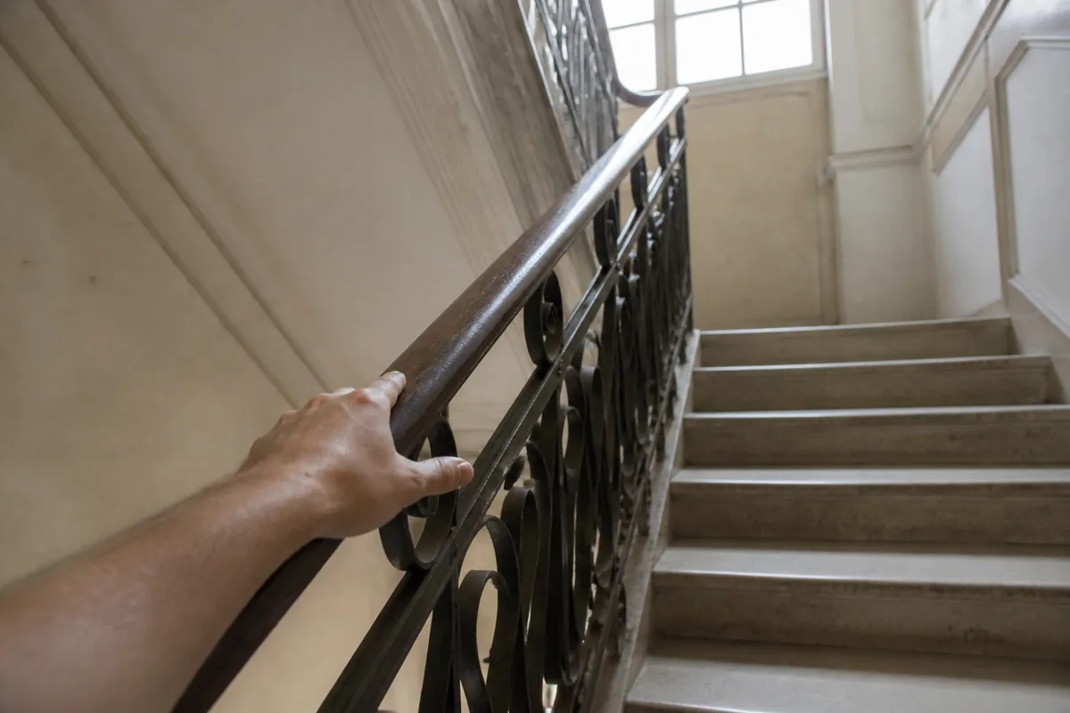 Escalier d&rsquo;immeuble emprunté à pied, main courante et lumière naturelle venant d&rsquo;une fenêtre