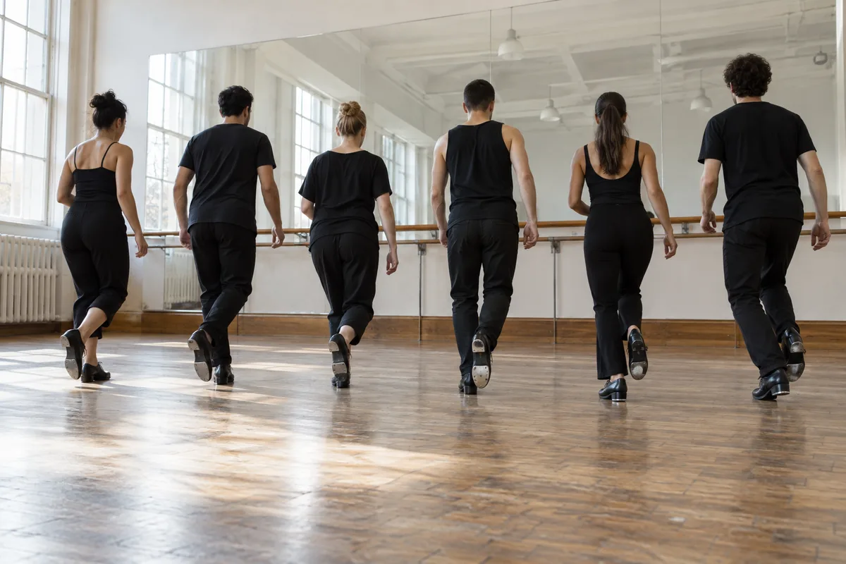 Groupe de danseurs vus de dos face au miroir d&rsquo;un studio pendant un stage de claquettes